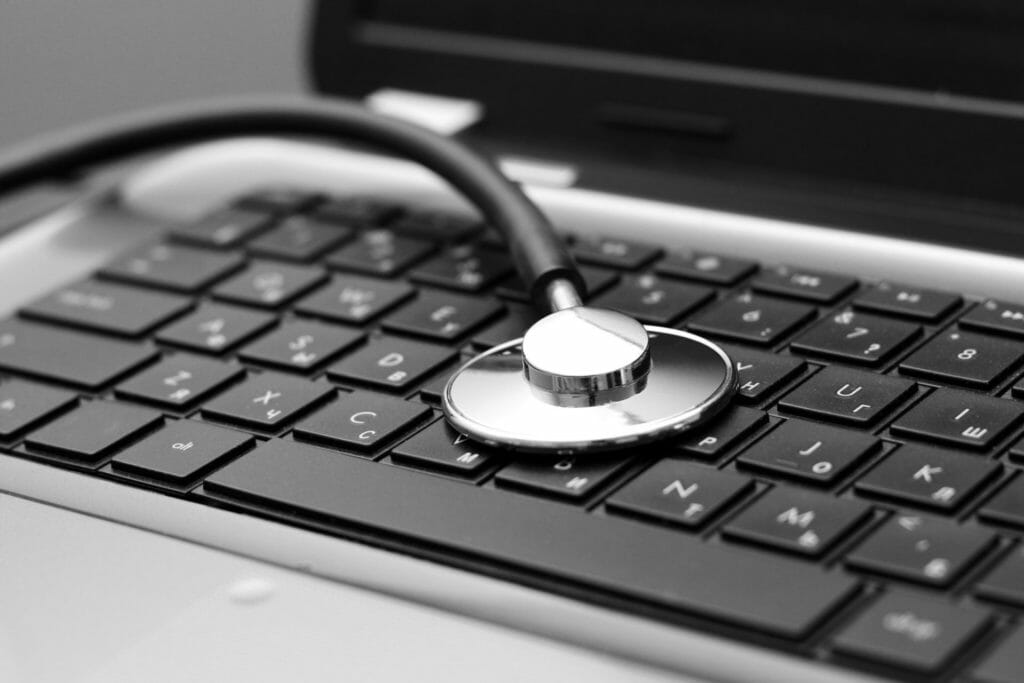 A stethoscope rests on the keyboard of a laptop, symbolizing healthcare technology, IT compliance, or digital health.