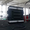 A large black equipment case with cables attached sits on a stage under a tent. Metal railings and a person in the background are visible.
