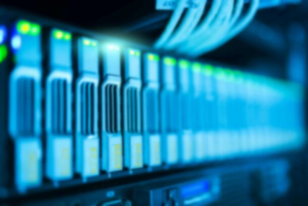 A row of blurred, illuminated server racks with network cables connected, indicating an active data center environment. A row of blurred, illuminated server racks with network cables connected, indicating an active data center environment.