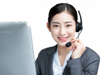 A woman wearing a headset and business attire sits in front of a computer, smiling at the camera.